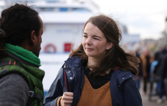 junge Frau mit Rucksack in einem Hafen im Gespräch mit einem jungen Mann